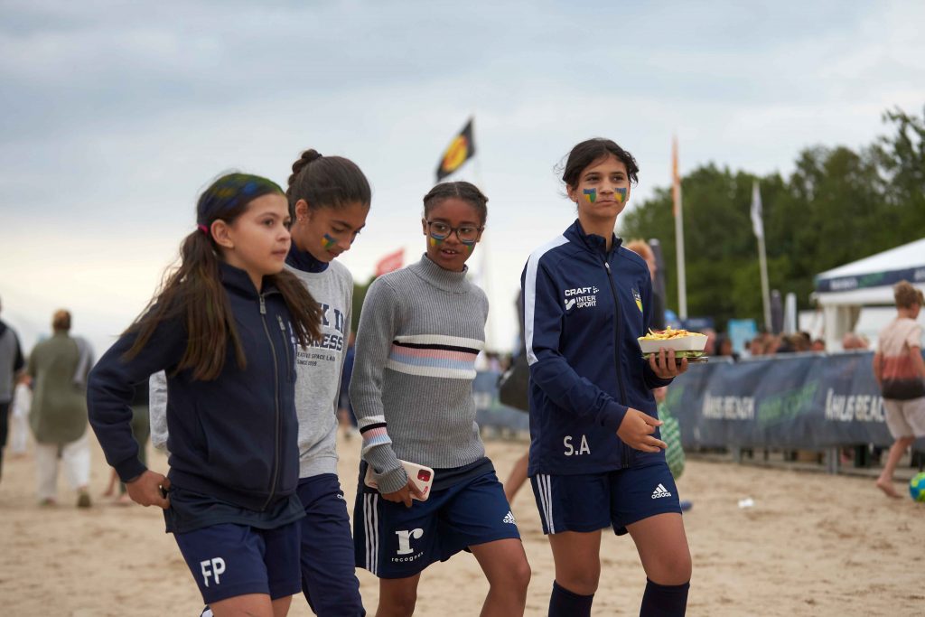 Fyra tjejer i tonåren klädda i matchkläder går i sanden på Åhus Beachfotboll festival