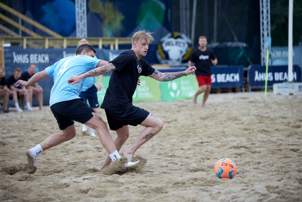 Två unga män kämpar för att ta fotbollen i en match på centercourten på Åhus Beachfotboll festival