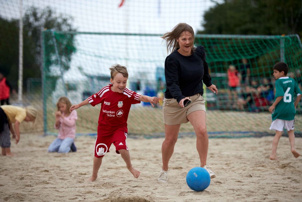 Mamma och son springer efter en fotboll på Åhus Beachfotboll festival