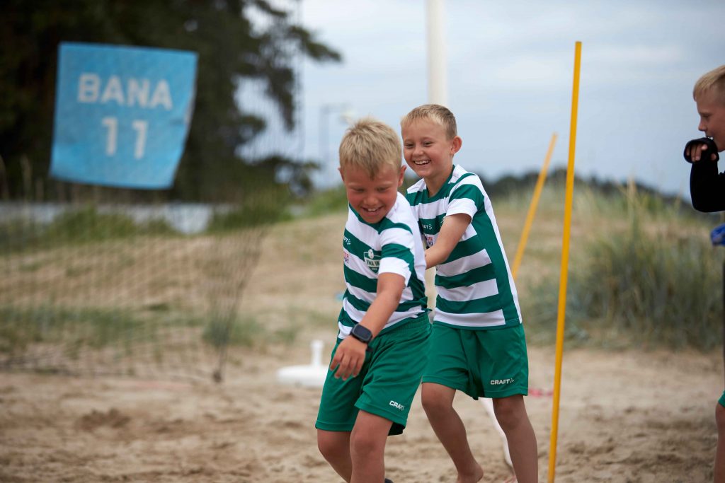 Glada killar skrattar och leker innan match på på Åhus Beachfotboll festival