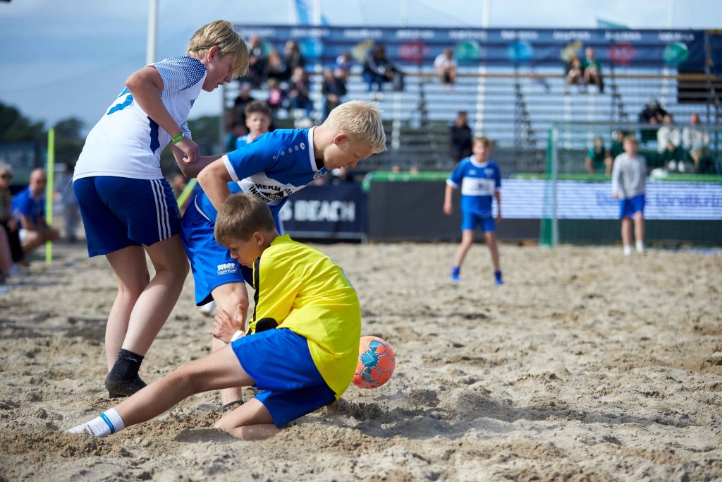Närkamp med tre unga killar som kämpar för att ta fotbollen på på Åhus Beachfotboll festival