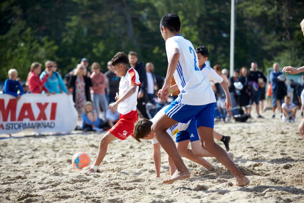 Unga män spelar fotbollsmatch i solen på Åhus Beachfotboll festival