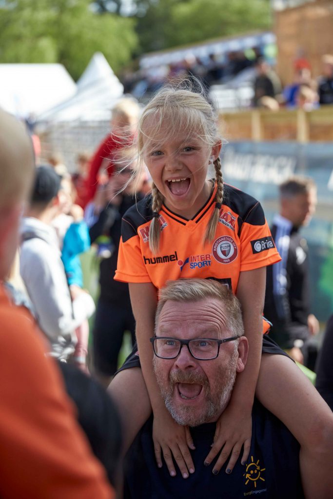 Glad flicka sitter på pappas axlar på Åhus Beachfotboll festival
