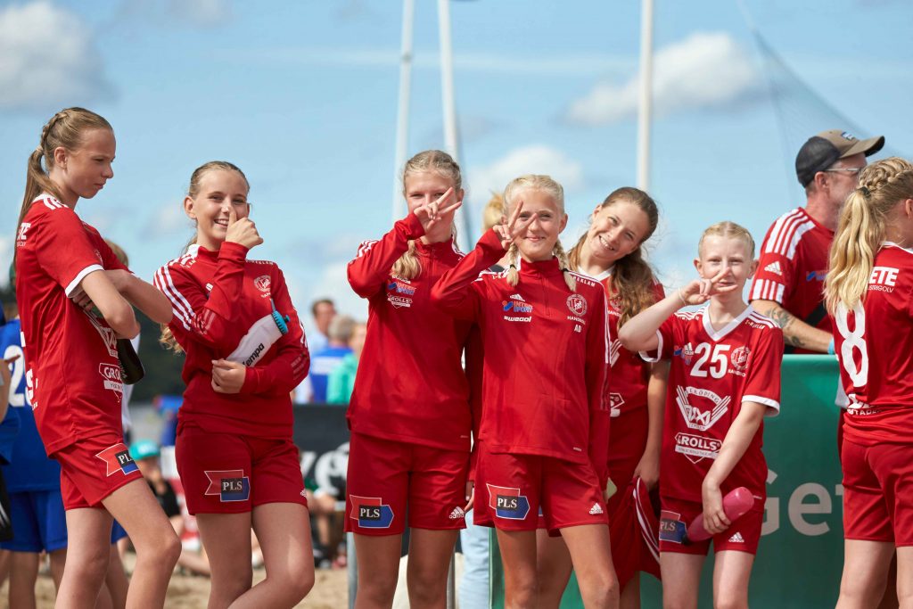 Tjejlag i rött poserar med segertecken framför kameran  på Åhus Beach festival