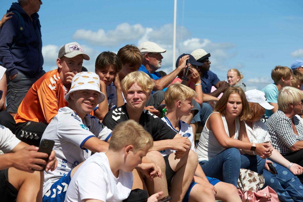 Publik sitter i solen på läktare på Åhus Beachhandbolls festival