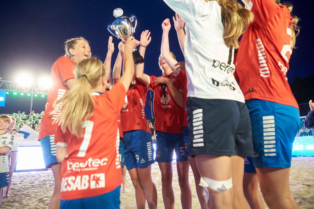 Lag hoppar och firar med sin pokal på Åhus Beach handbolls festival